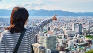 ストライプのトップスを着た後ろ姿の若い人が高台から街を指す