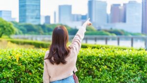 ベージュのニットを着た後ろ姿の若い人が都市を指す