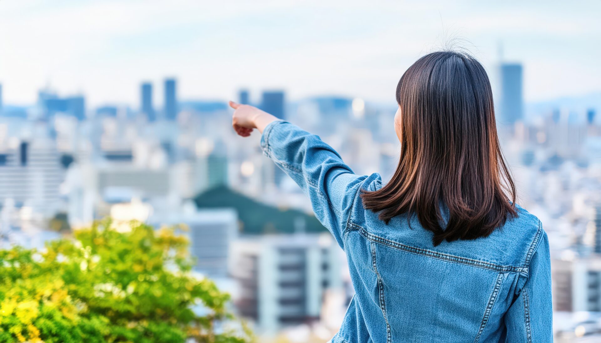 デニムジャケットを着た後ろ姿の若い人が街を指す