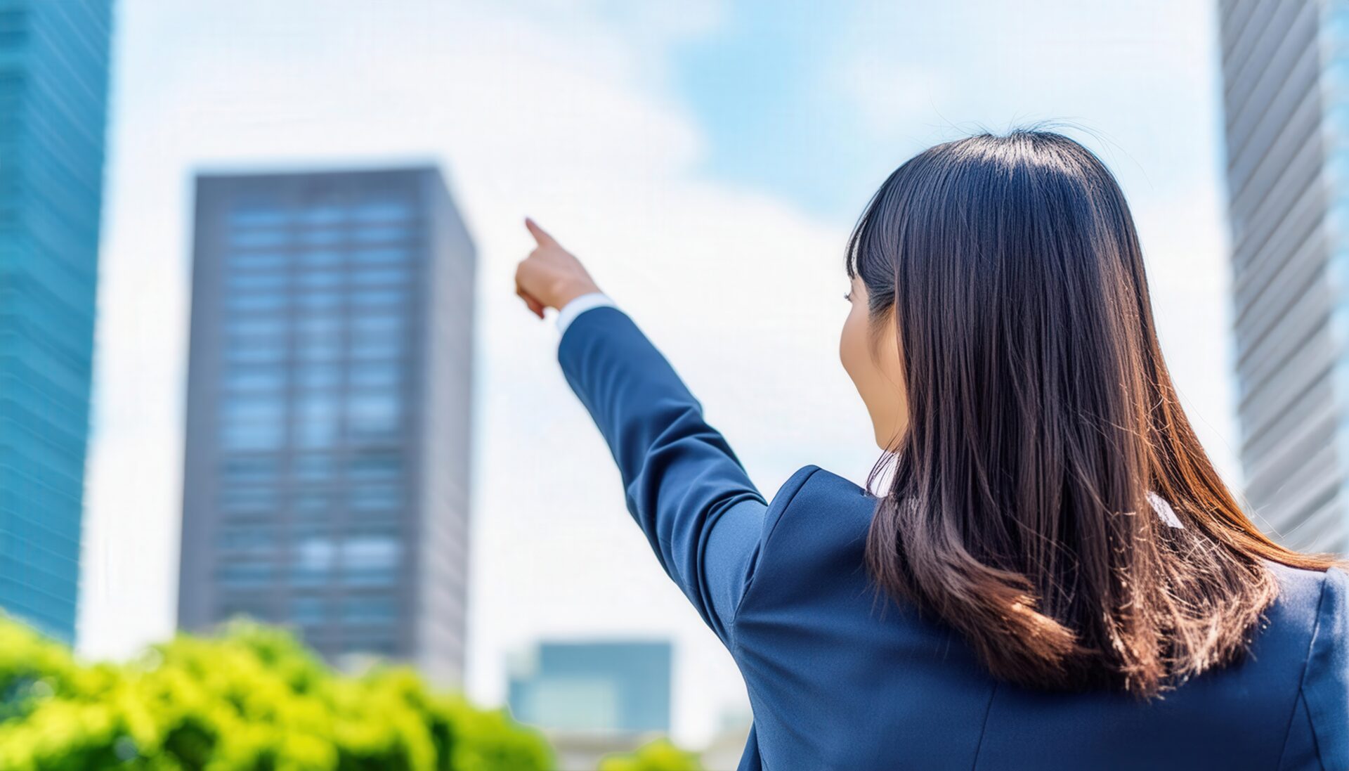 後ろ姿のスーツ姿の人が高層ビルを指す