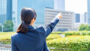 後ろ姿のスーツ姿の人がオフィス街を指す