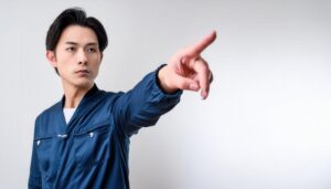 白背景で青い作業服を着た男性が指をさす