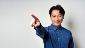 白背景で青いシャツを着た若い男性が指をさす