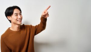 白背景でブラウンのセーターを着た若い男性が正面を指さす