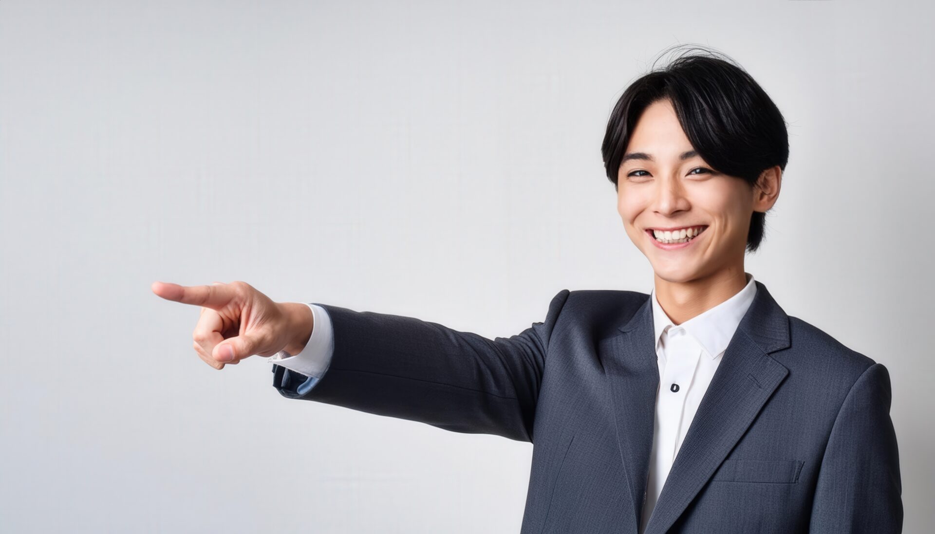 白背景でグレースーツを着た若い男性が右を指さす