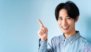 青背景でストライプシャツを着た若い男性が指をさす