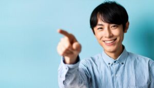 青背景でストライプシャツを着た若い人がこちらを指さす