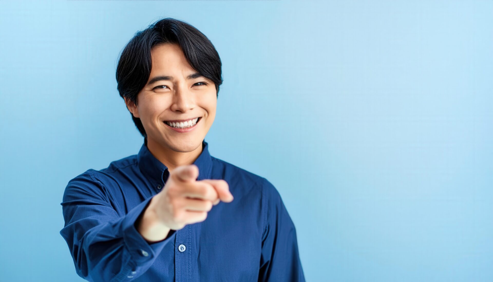 青背景でネイビーのシャツを着た若い人がこちらを指さす