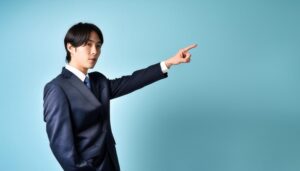 青背景でネイビースーツを着た若い人が斜め前を指さす