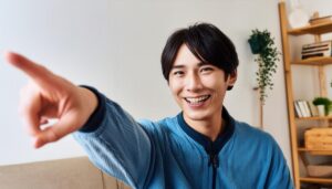 室内でブルーのジャケットを着た若い男性がこちらを指さす