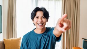 室内でブルーのTシャツを着た笑顔の若い男性がこちらを指さす