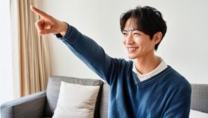 室内でネイビーのセーターを着た若い男性が右上を指さす