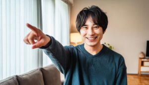 室内でダークグリーンのセーターを着た若い男性がこちらを指さす