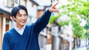 街中でネイビーのセーターを着た若い男性が前方を指さす