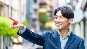 街中でネイビーのジャケットを着た若い男性が右を指さす