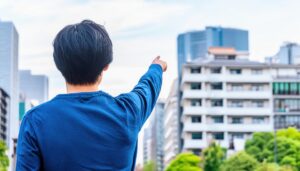 都市の高層ビルを背景に指をさす後ろ姿の若い男性