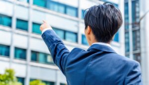 外のビルを指し示す後ろ姿の若い男性