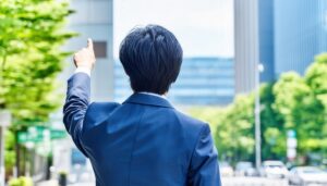 青空の下でビルを指差す後ろ姿の若い男性