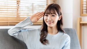 ソファで水色のセーターを着て敬礼する人物