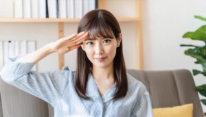 室内で水色の服を着て敬礼する人物