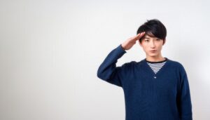 白背景でネイビーのセーターを着て敬礼する人物