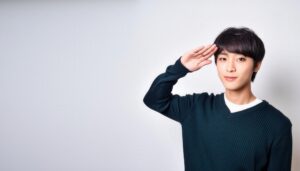 白背景で青いセーターを着て敬礼する人物