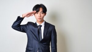 白背景で黒いスーツを着て敬礼する人物