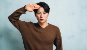 青背景でブラウンのセーターを着て敬礼する人物