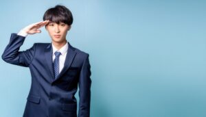 青背景でネイビーのスーツを着て敬礼する人物