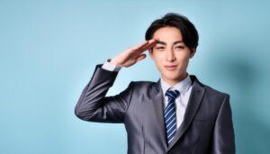 青背景でグレーのスーツを着て敬礼する人物