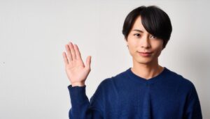 白背景で挙手する青いセーターの男性