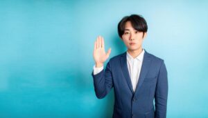 青い背景で挙手するジャケット姿の人物