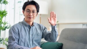 室内で挙手するメガネシャツの人物