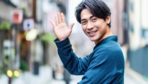 街中で手を上げて振り向く青いシャツの人物