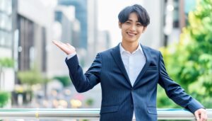 街のビルを背景に片手を上げるスーツ姿の人