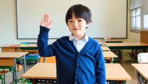 教室の机の前で片手を上げる子供
