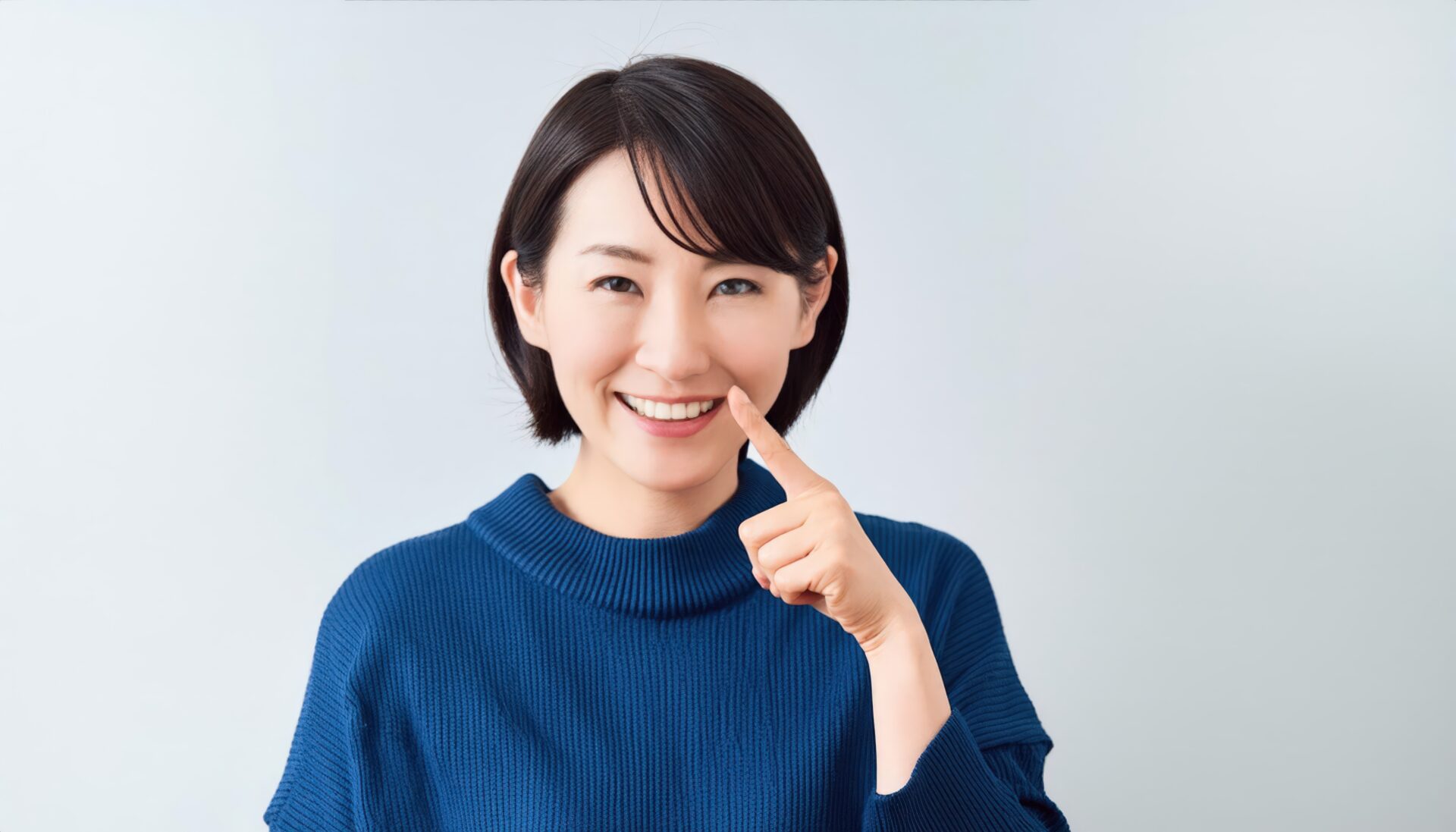 青いセーターを着て指を口元に当てる人