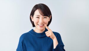 青いセーターを着て指を口元に当てる人