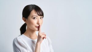 白いブラウスで口止めの仕草をする人