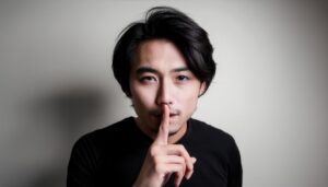 モノトーンの背景で静かにとジェスチャーする髭の男性