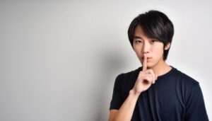 ダークカラーのTシャツで口に指を当てて黙る20代の男性