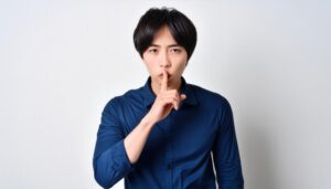 青いシャツで口に指を当てて黙る20代の男性