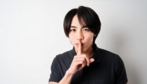 ダークカラーのポロシャツで口に指を当てて黙る20代の男性