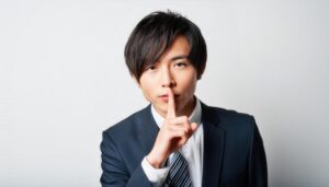 ネイビースーツで口に指を当てて黙る20代の男性