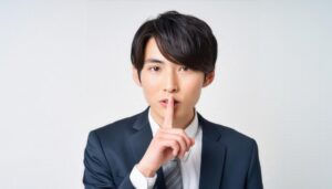 黒いスーツで口に指を当てて黙る20代の男性