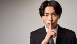 黒いスーツで口に指を当てて黙る20代の男性