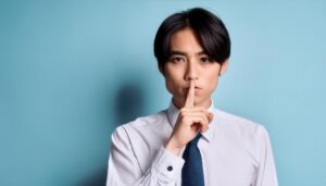 口元に指を当てて静かにするジェスチャーをする若いビジネスマン