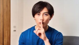 室内で口元に指を当て静かにするポーズをとる若者