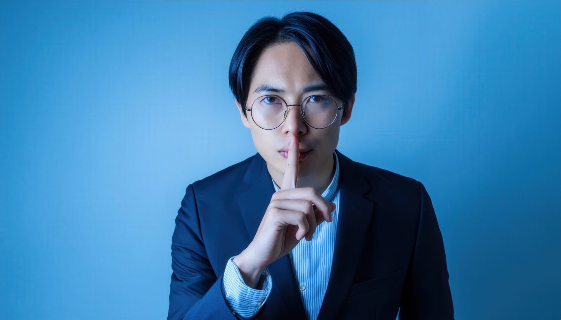 静かにのジェスチャーをする黒髪の若いビジネスマン