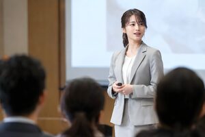 ホールの壇上でクリッカーを手に発表する20代女性